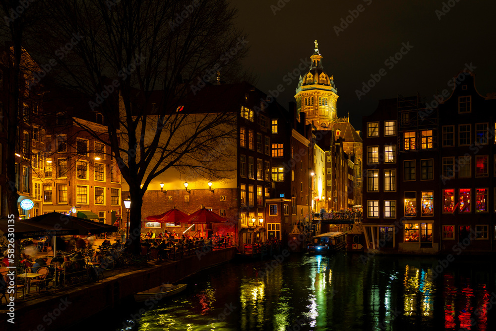 Amsterdam nightscape skyline, lighted castle, canal, buildings, water reflections, and busy street at night in Netherlands, vibrant long exposure photography