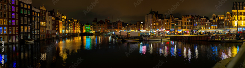 Amsterdam nightscape skyline, canal, buildings, boats, water reflections, and busy street at night in Netherlands, vibrant long exposure photography
