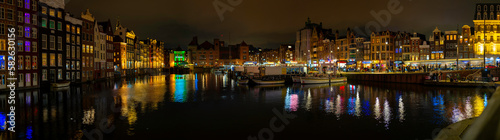 Amsterdam nightscape skyline, canal, buildings, boats, water reflections, and busy street at night in Netherlands, vibrant long exposure photography