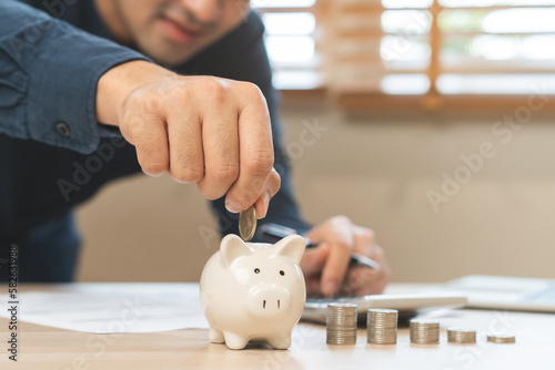 Close up hand of asian young businessman, male putting coin into a piggy ceramic for saving cost, financial plans to spend enough money on his income for saving money and payment, finance people. photo