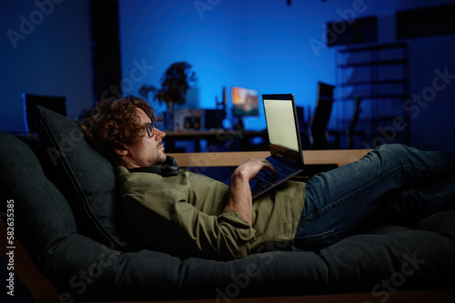 Man IT administrator rest on sofa with laptop computer lying on sofa photo