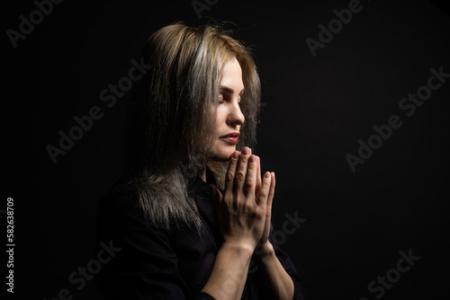 Woman praying with hands together on black background
