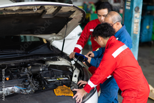 Professional team mechanic car repair service and checking car engine by Diagnostics Software computer. Expertise mechanic working in automobile repair garage.