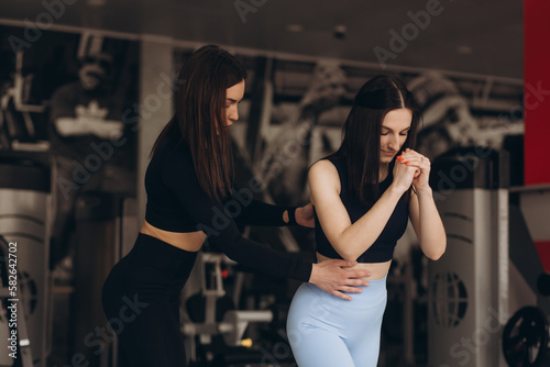 Female personal trainer corrects and advises her brunette client during training in the gym.