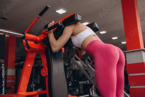 a girl with a sporty figure squats in the gym on a simulator