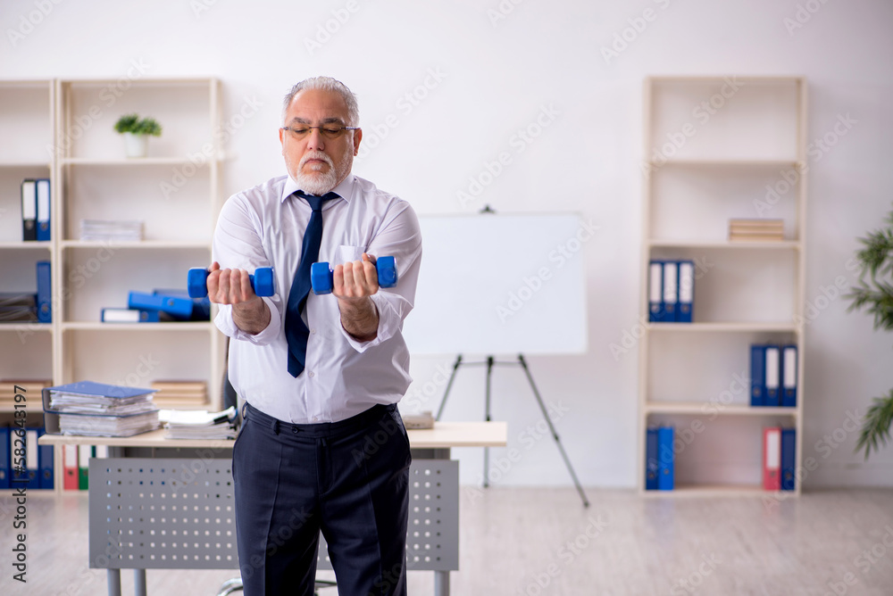 Old male employee doing sport exercises at workplace