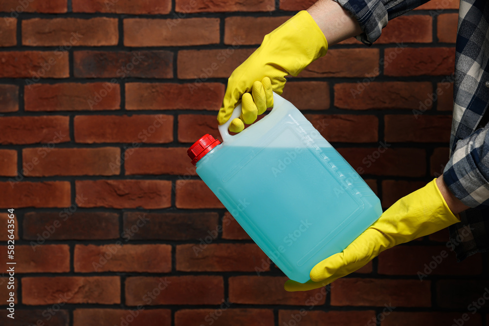 Man in rubber gloves holding canister with blue liquid near brick wall, closeup. Space for text