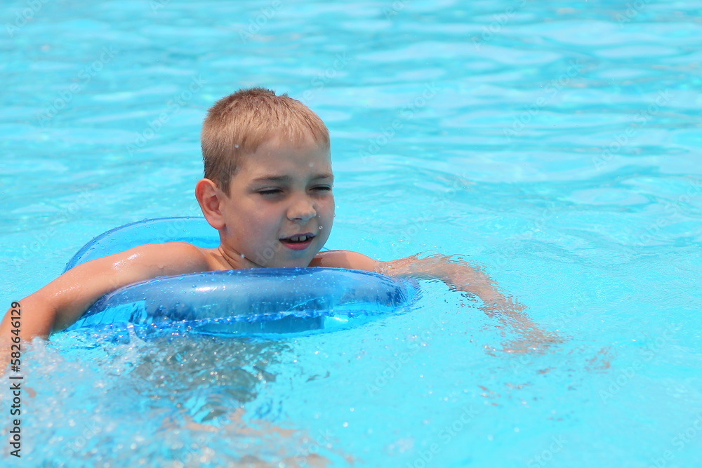 Happy little boy with blue life ring has fun in the swimming pool