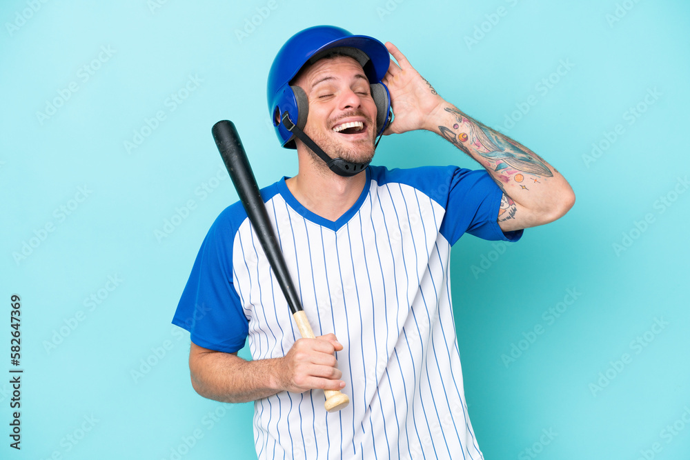 Baseball player with helmet and bat isolated on blue background smiling a lot Baseball player with helmet and bat isolated on blue background smiling a lot