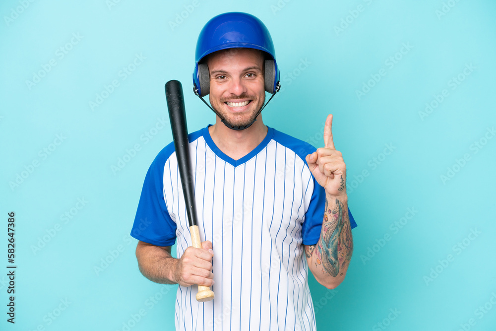 Baseball player with helmet and bat isolated on blue background showing and lifting a finger in sign of the best Baseball player with helmet and bat isolated on blue background showing and lifting a finger in sign of the best