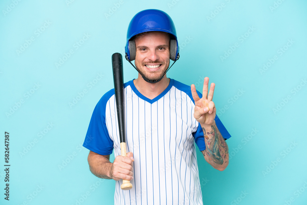 Baseball player with helmet and bat isolated on blue background happy and counting three with fingers Baseball player with helmet and bat isolated on blue background happy and counting three with fingers