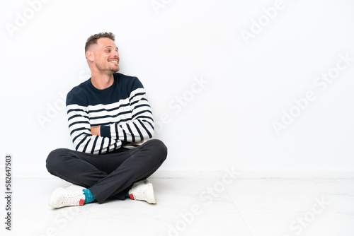 Young man sitting on the floor isolated on white background happy and smiling