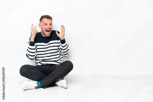 Young man sitting on the floor isolated on white background with surprise facial expression