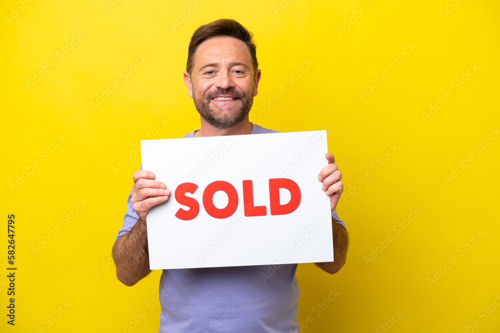 Middle age caucasian man isolated on yellow background holding a placard with text SOLD with happy expression Middle age caucasian man isolated on yellow background holding a placard with text SOLD with happy expression