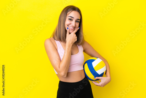 Young woman playing volleyball isolated on yellow background happy and smiling