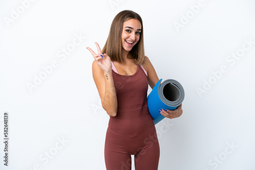 Young sport caucasian woman going to yoga classes isolated on white background smiling and showing victory sign © luismolinero