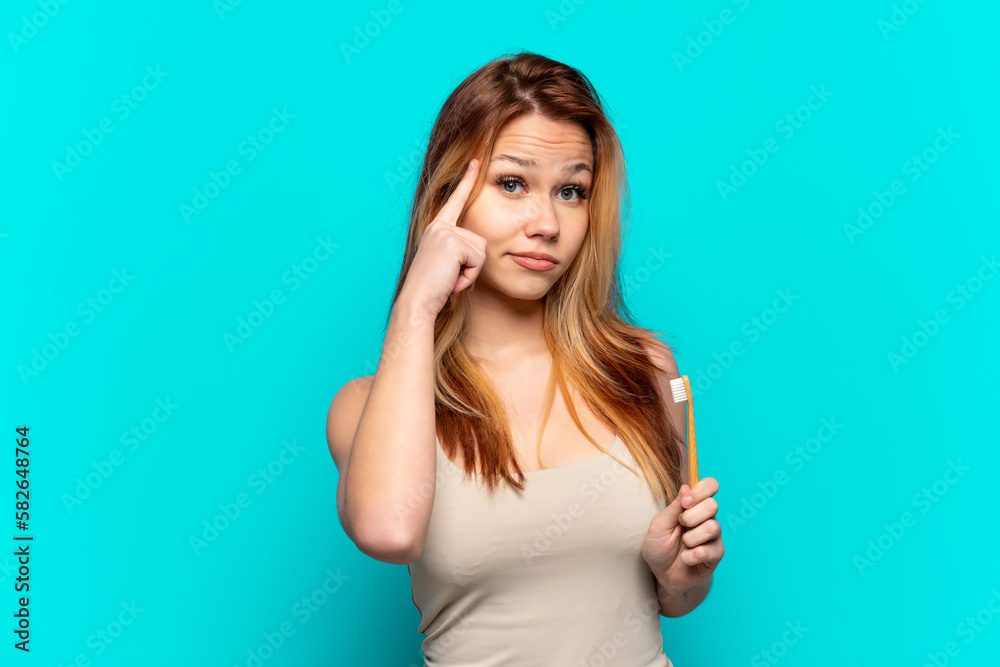 Fototapeta premium Teenager girl brushing teeth over isolated blue background thinking an idea