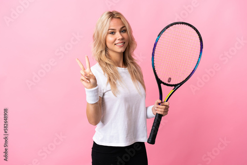 Young Russian woman playing tennis isolated on purple background smiling and showing victory sign © luismolinero
