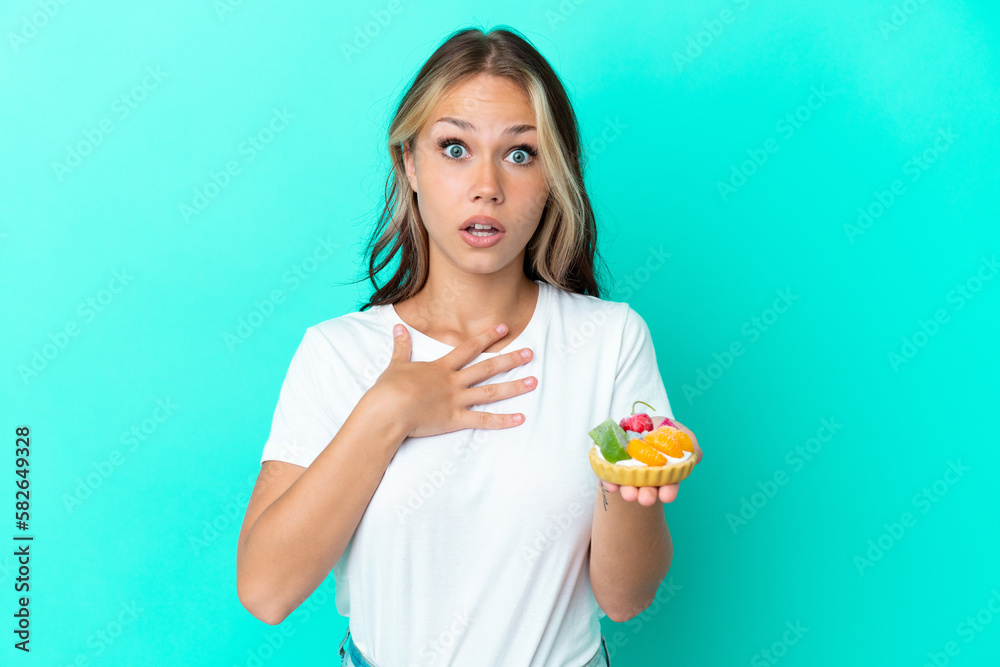 Young Russian woman holding a fruit sweet isolated on blue background surprised and shocked while looking right Young Russian woman holding a fruit sweet isolated on blue background surprised and shocked while looking right