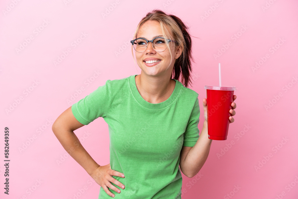 Young Russian woman holding a refreshment isolated on pink background posing with arms at hip and smiling Young Russian woman holding a refreshment isolated on pink background posing with arms at hip and smiling