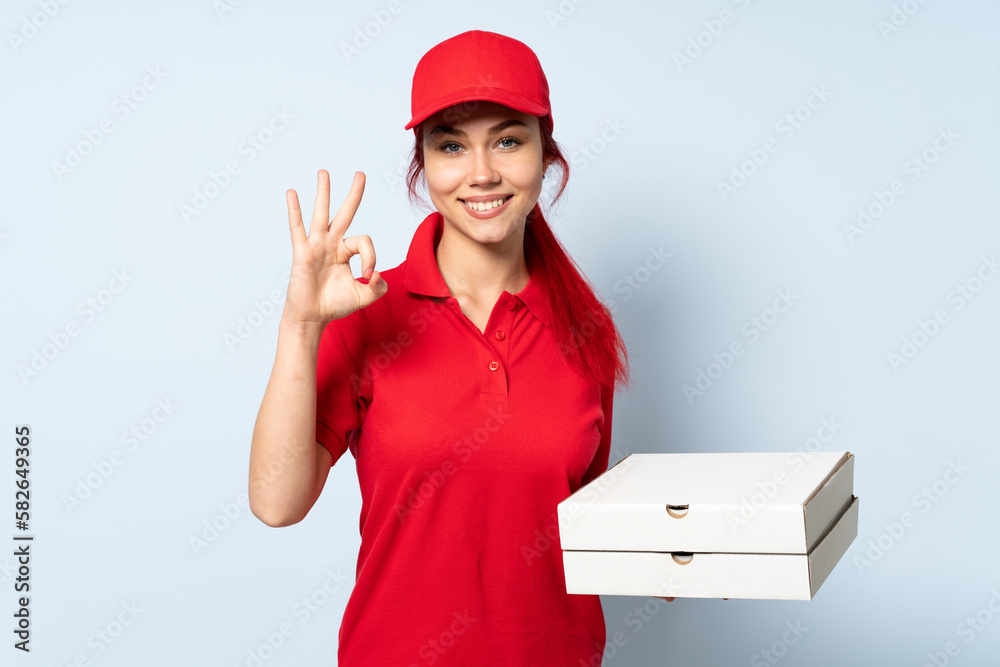 Pizza delivery girl holding a pizza over isolated background showing ok sign with fingers Pizza delivery girl holding a pizza over isolated background showing ok sign with fingers
