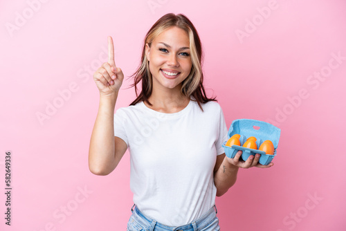 Young Russian woman holding eggs isolated on pink background pointing up a great idea