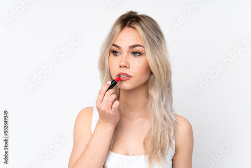 Teenager blonde girl over isolated white background holding red lipstick