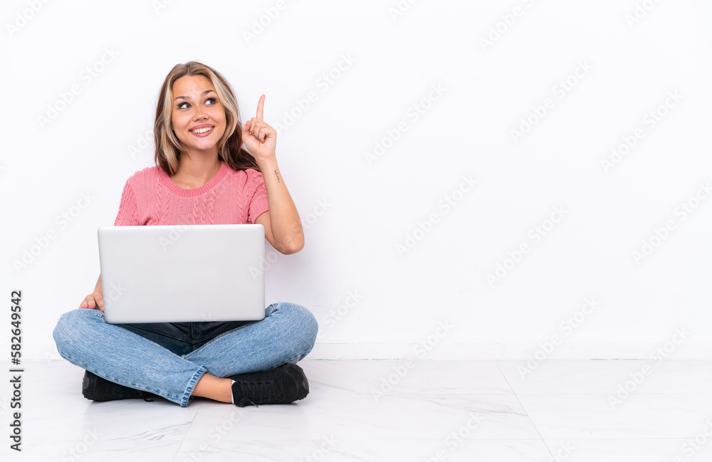Young Russian girl with a laptop sitting on the floor isolated on white background intending to realizes the solution while lifting a finger up Young Russian girl with a laptop sitting on the floor isolated on white background intending to realizes the solution while lifting a finger up