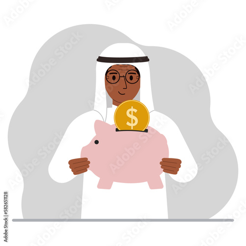 Happy muslim man holds a piggy bank, a coin falls into the piggy bank. The concept of saving finance, savings, investing finances.