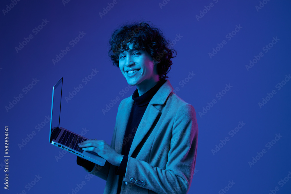 A man with a laptop in his hands and a jacket, smile, blue light glasses, Blue Perennial color, cyber security, technology, open laptop copy space, trendy neon, freelancer, purple light - obrazy, fototapety, plakaty 