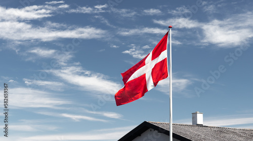 The national flag of Denmark: red with a white Nordic cross, mounted on top of the house, blue sky in the background