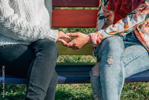 clasped hands of lesbian women on rainbow bench. pride concept