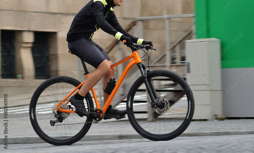 Naklejka premium Person riding a orange bicycle on a city street, motion blur, speed