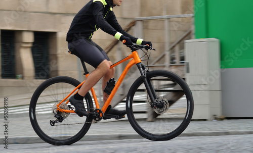 Fototapeta Naklejka Na Ścianę i Meble -  Person riding a orange bicycle on a city street, motion blur, speed