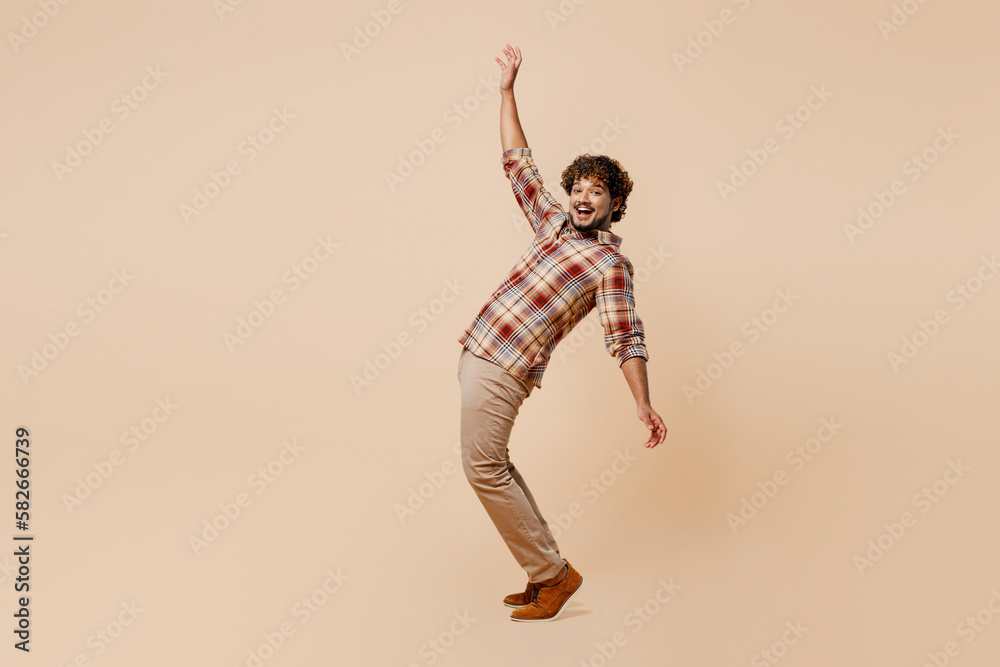 Full body side view young Indian man wear brown shirt casual clothes leaning back with outstretched hands stand on toes isolated on plain pastel light beige background studio People lifestyle concept Full body side view young Indian man wear brown shirt casual clothes leaning back with outstretched hands stand on toes isolated on plain pastel light beige background studio People lifestyle concept