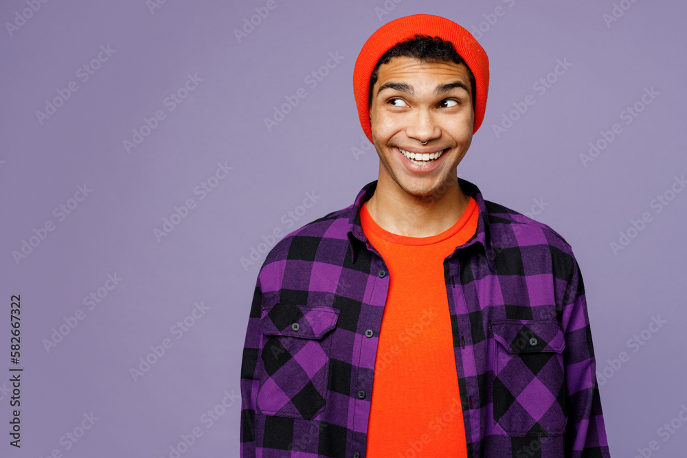 Fototapeta premium Young surprised shocked man of African American ethnicity wearing casual shirt orange hat look aside on workspace area mock up isolated on plain pastel light purple color background studio portrait.
