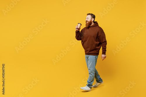 Fototapeta Naklejka Na Ścianę i Meble -  Full body young redhead caucasian man wear brown hoody casual clothes hold takeaway delivery craft paper brown cup coffee to go isolated on plain yellow background studio portrait. Lifestyle concept.