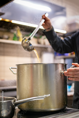 chef cooking tasty soup in big pot on restaurant kitchen