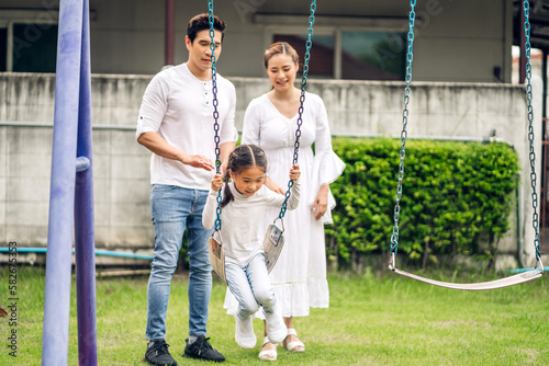 Portrait of enjoy happy love asian family father and mother with little asian girl smiling playing and pushing daughter on the swing moments good time at playground #582675353