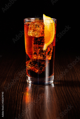 Cola with a slice of lemon and ice in a tall glass. Selective focus, black background.