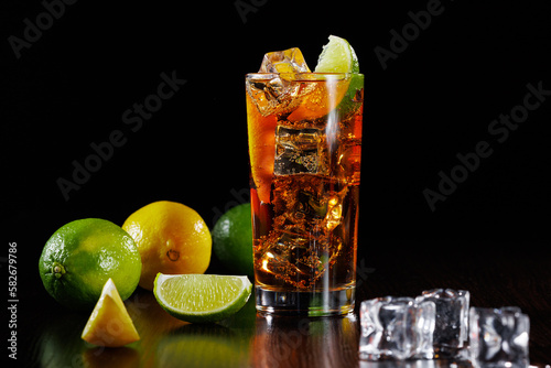 Carbonated cola drink with lime slice and ice in a tall glass on a black background. Selective focus.