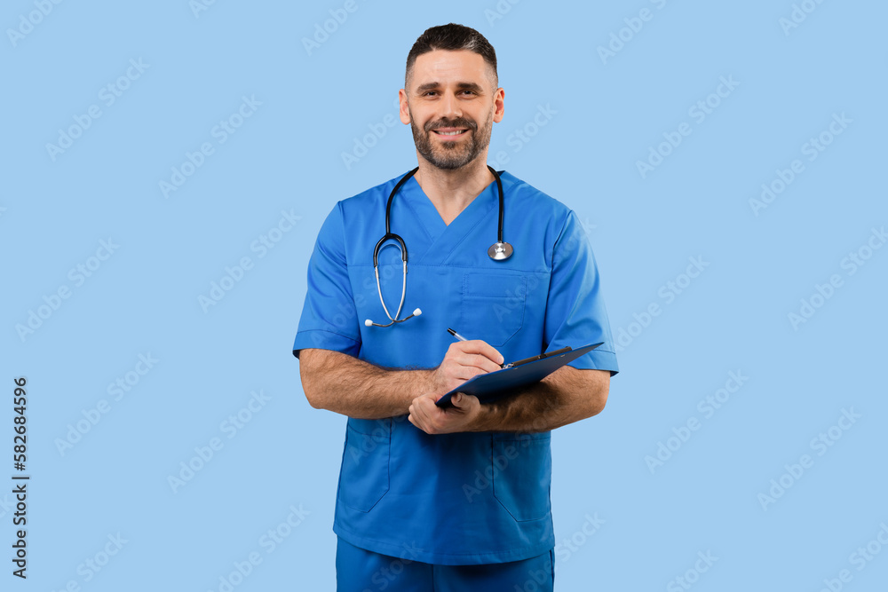 Middle aged male doctor in uniform working with patient anamnesis, standing over blue background and smiling at camera - obrazy, fototapety, plakaty 