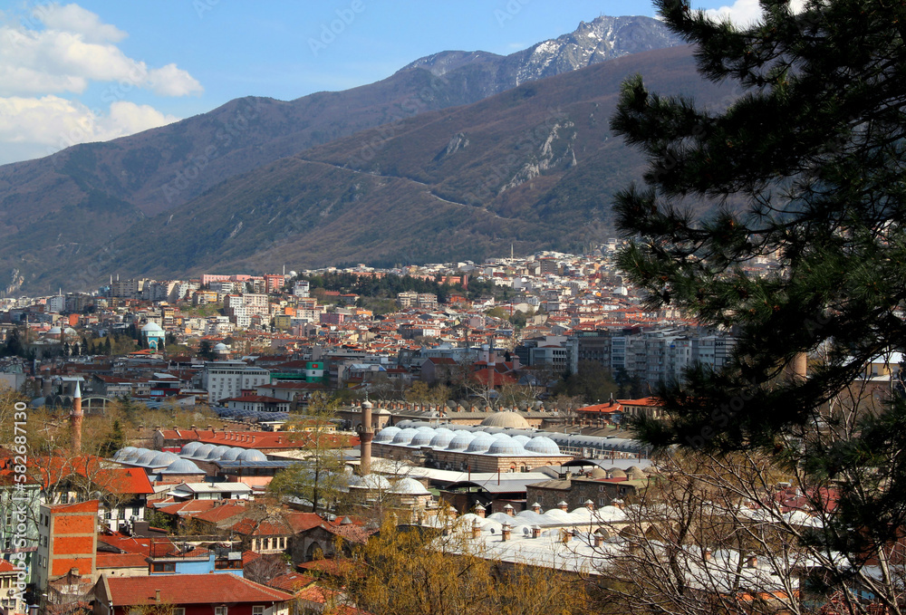 A panoramic view of the city of Bursa (Turkey) with many mosques, hans and Uludag mountain in the background against a blue sky with clouds	