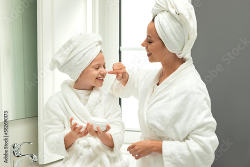 Smiling european millennial woman and little girl in bathrobes and towel have fun, take care of beauty