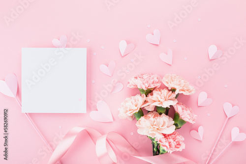 Bouquet of beautiful pink carnation flowers, hearts and greeting card on pastel table for Happy mothers day. Flat lay. © juliasudnitskaya