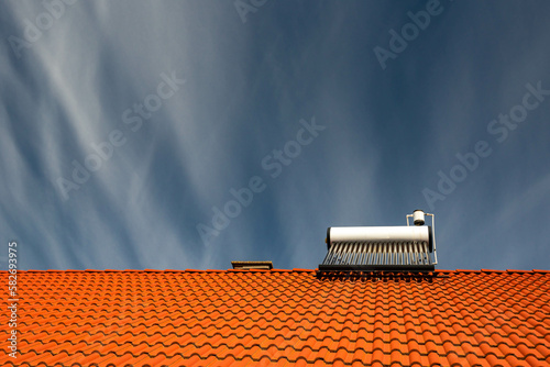 Front view of a solar water heater boiler on rooftop, dark blue sky with white washed clouds, space for text.