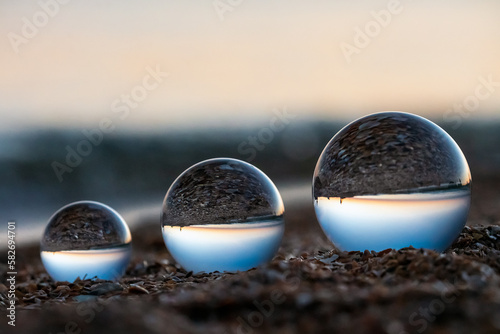 Glass lens globes on sandy beach on sea background at sunset. Beauty, fancy, family, evolution, increase and growth, rise and increment concept.