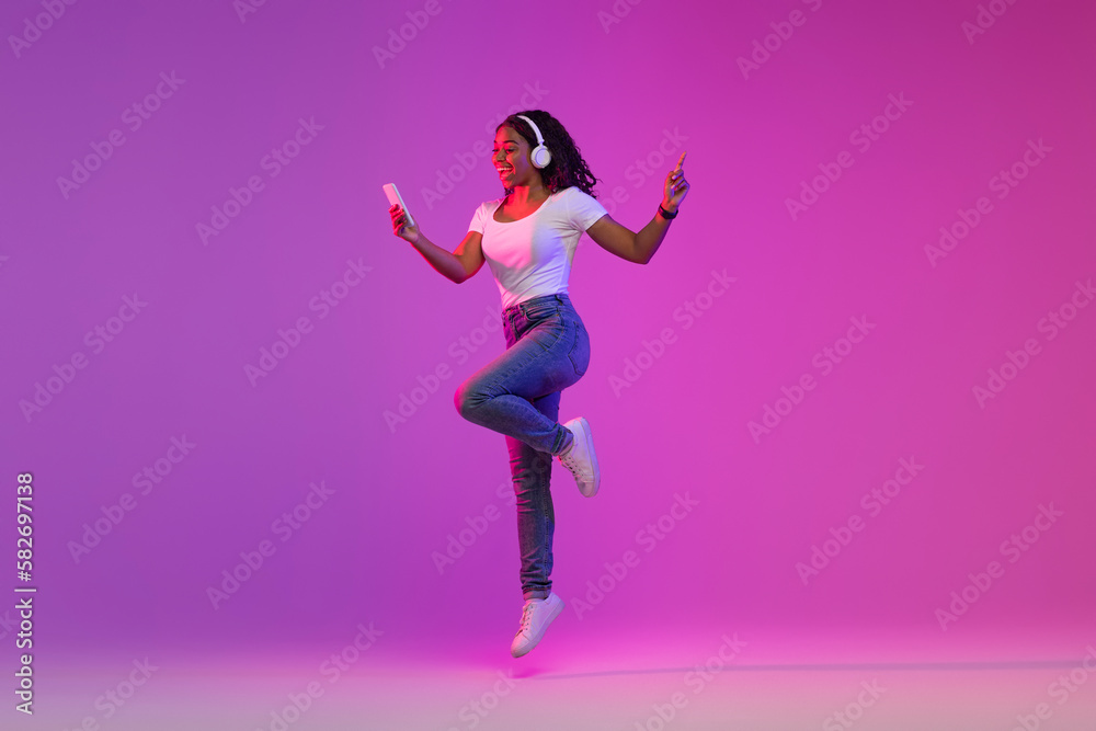 Cheerful Young Black Female In Wireless Headphones Jumping With Smartphone In Hand