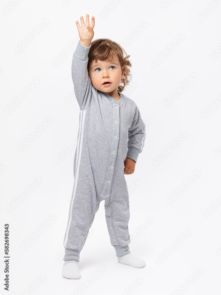 Gymnastics, fitness, exercise. A 1-2-year-old child goes in for sports in a gray jumpsuit, pulls his hand up on a white background. Gymnastics, fitness, exercise. A 1-2-year-old child goes in for sports in a gray jumpsuit, pulls his hand up on a white background.