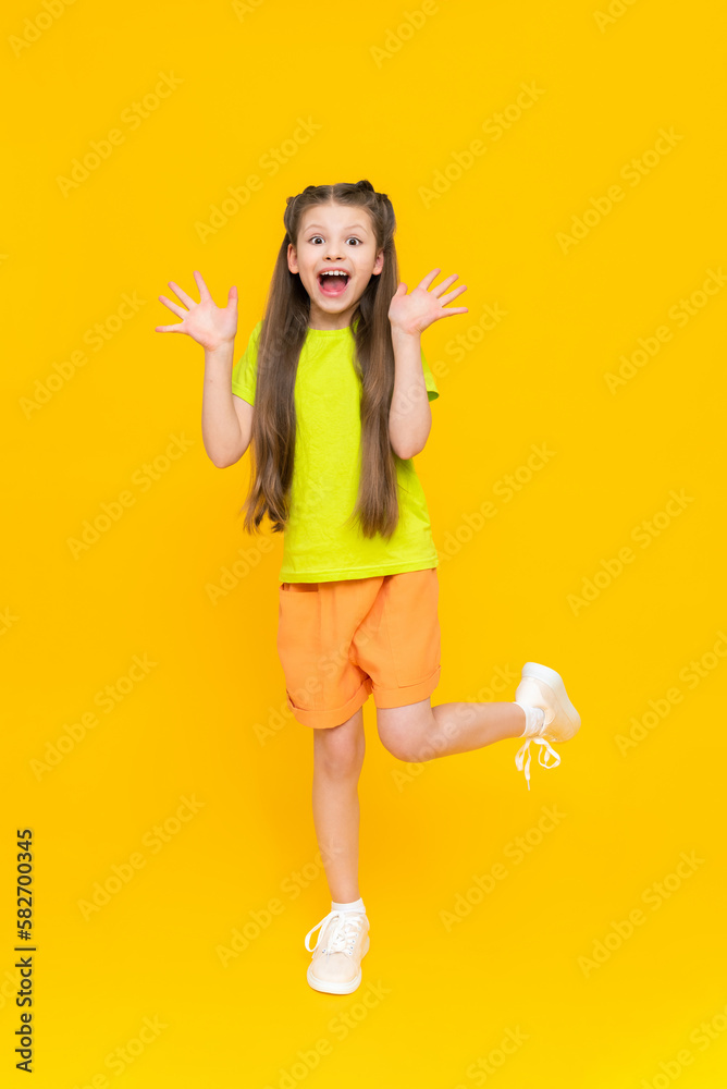 A child in shorts and a T-shirt. Happy childhood. A little girl with long hair enjoys the warmth in summer clothes on a yellow isolated background.